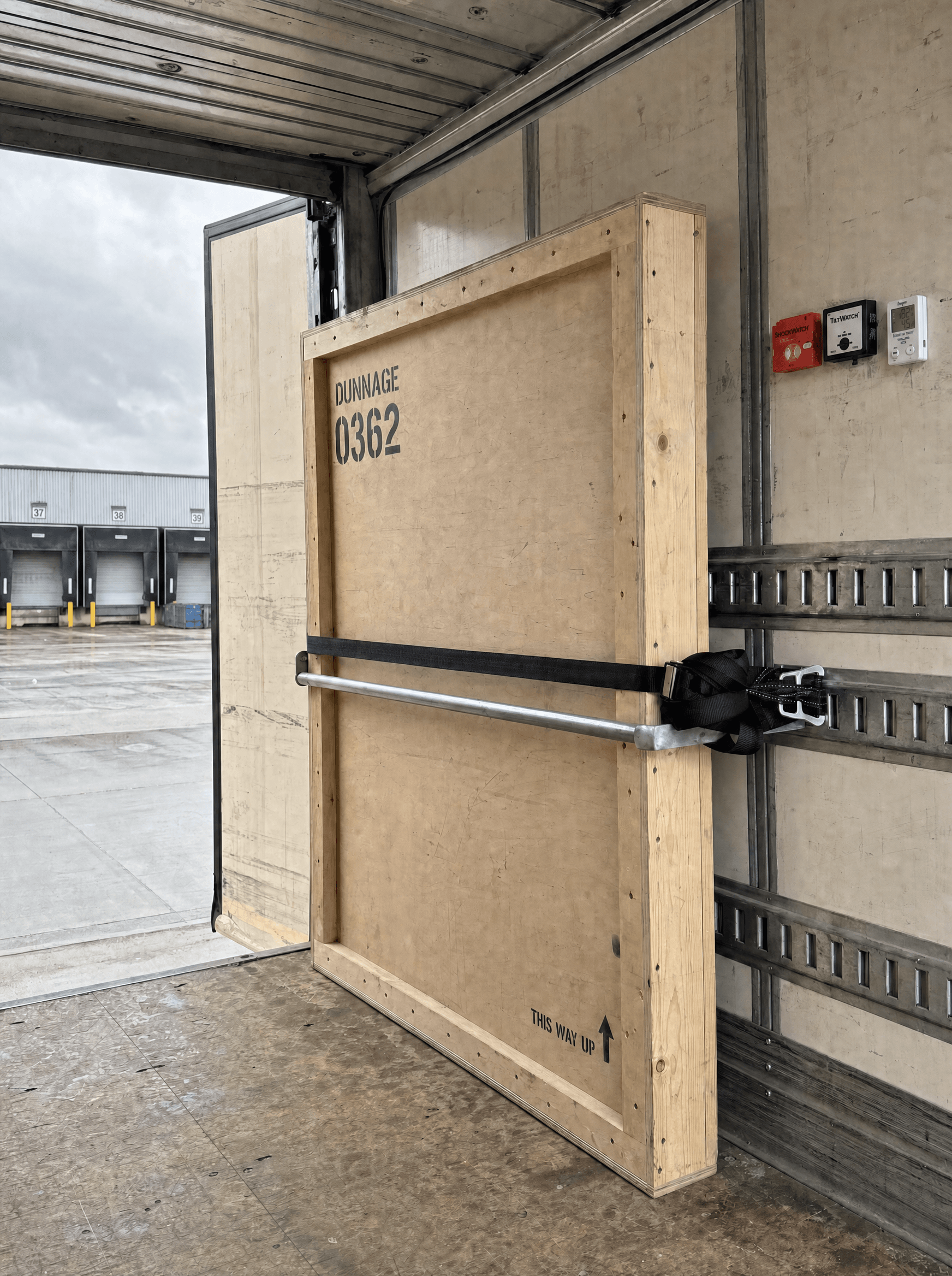 A single stencilled Dunnage crate strapped alone in an empty box truck hold with shock and tilt indicators fitted