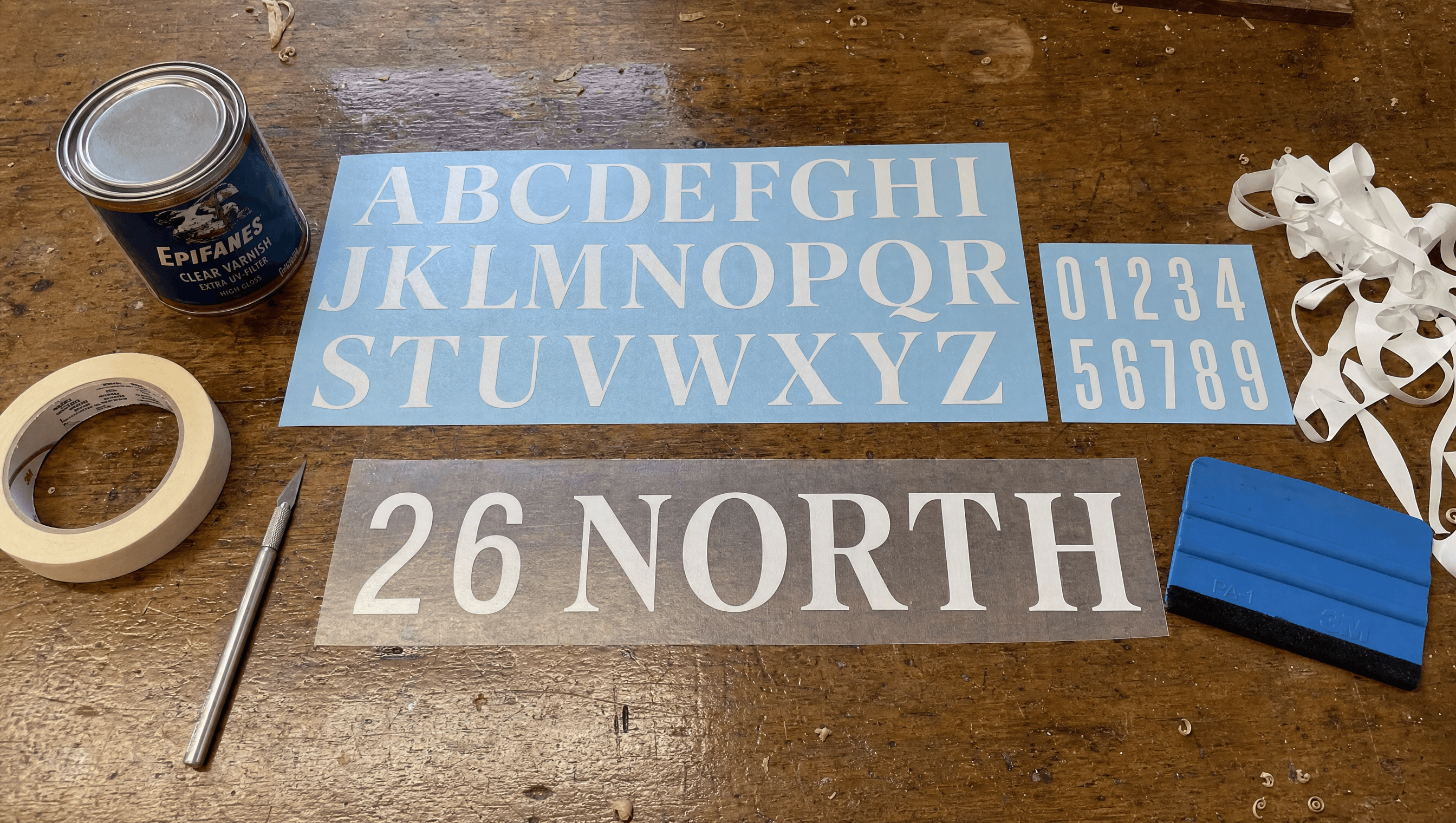 26 North vinyl transfer lettering sheets on a boatyard workbench, the name part-weeded