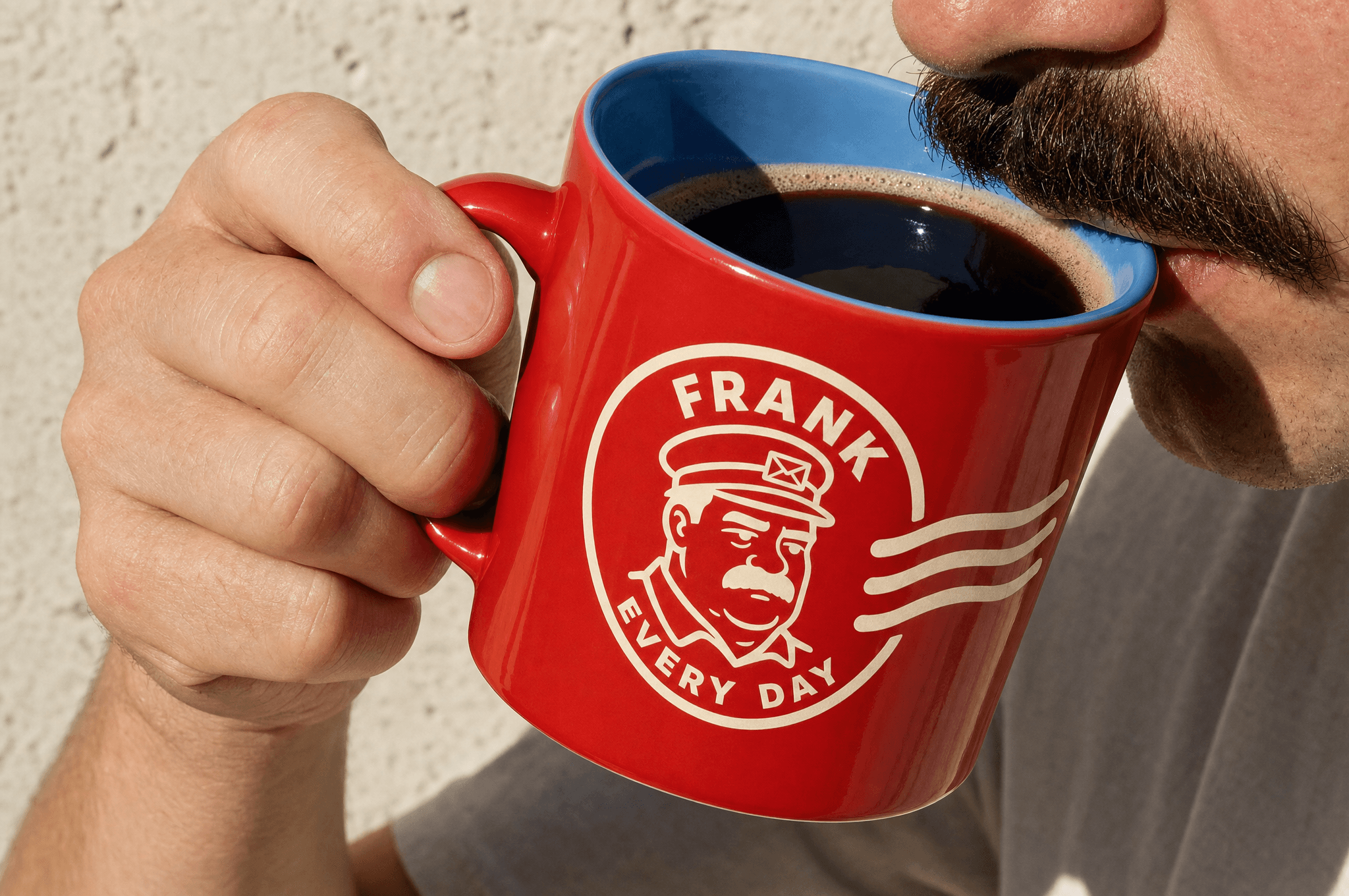 A red FRANK mug with a sky blue interior, held mid-sip